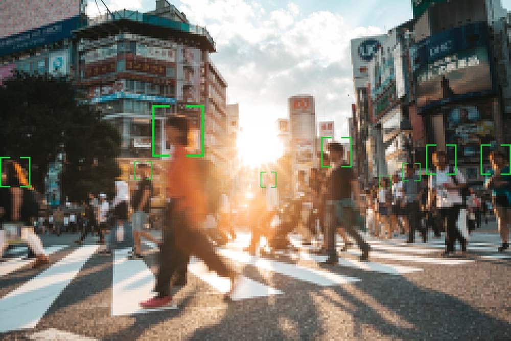 A facial recognition viewfinder is pointed at passers-by crossing the street. The image is symbolic of the question: What is tracking?
