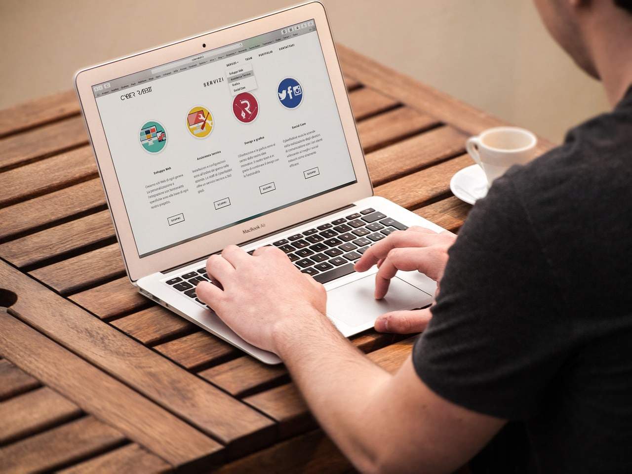 A man is sitting at the opened laptop. You can see a landing page on it.